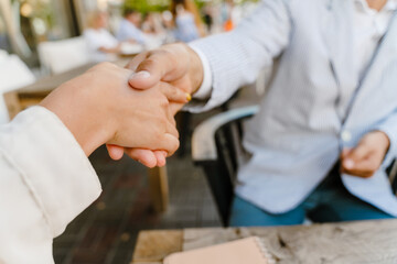 Young man and woman shaking hands during business meeting at cafe