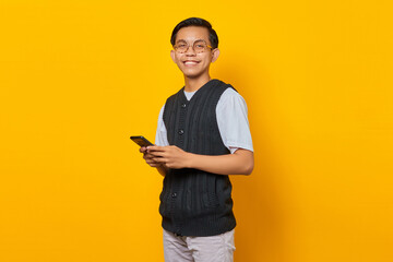 Portrait of smiling young handsome man using smartphone on yellow background