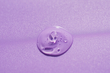 Transparent drop of cosmetic product serum gel. Liquid texture with bubbles on lilac background in top view