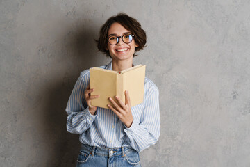 Young woman wearing eyeglasses smiling while reading book