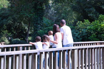 Happy, large family of five seen from the back, looking out over a wooden bridge. Parents with...