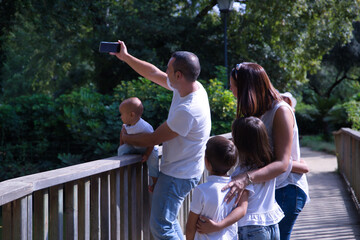 Happy, large family of five taking a selfie on a wooden bridge. Parents with three children, one of...