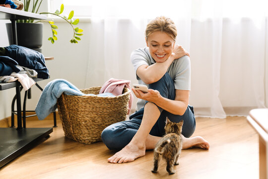 Ginger mature woman playing with kitten while doing housework