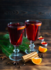 Hot mulled wine with cinnamon and star anise in transparent glasses on a dark wooden table. Cinnamon tubes, tangerine slices and candles in the background
