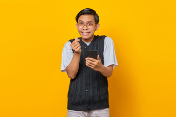 Portrait of cheerful Asian young man showing finger heart and holding smartphone