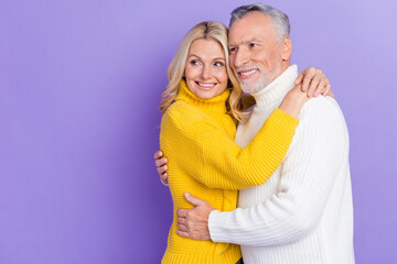 Photo of funny sweet senior husband wife dressed knitwear sweaters hugging looking empty space smiling isolated violet color background