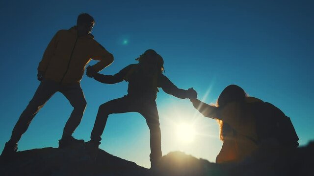 help team concept. team silhouette of climber stretching a helping hand to a friend. business teamwork success concept. silhouette business travel three tourists pull a helping hand sunlight