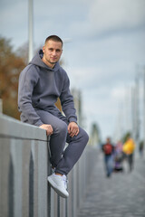 A young man in a tracksuit stands in a city park
