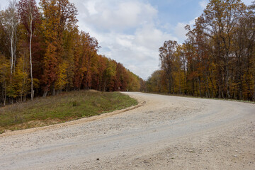 Autumn, dirt road through the park, colorful foliage on the crowns of trees, clear morning air, panoramic view.