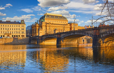 Fototapeta premium Prague, Czech Republic. View at Legion bridge on river Vltava. National Theatre (Narodni Divadlo) on embankment in sunbeams of evening sunset sunlight.