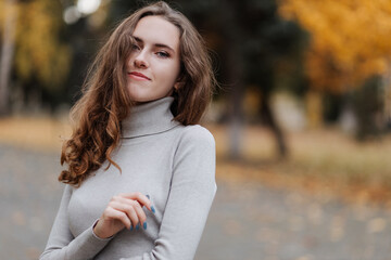 Portrait of young smiling girl in a gray dress at autumn park 