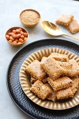  Indian makar sankranti festival food oe sweets. Tilgul in a small brass plate. Tilgul is made out of sesame seeds, peanuts, and jaggery. Til gul chikki or sesame candy. Copy Space.