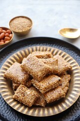  Indian makar sankranti festival food oe sweets. Tilgul in a small brass plate. Tilgul is made out of sesame seeds, peanuts, and jaggery. Til gul chikki or sesame candy. Copy Space.