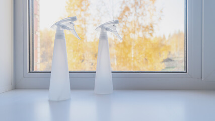 Two white sprayers for indoor plants on the windowsill, outside the window autumn nature with yellow leaves
