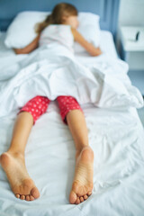 Girl's feet covered with white bed sheet, sleeping in a comfortable bed