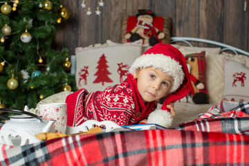 Cute toddler child, boy in a christmas outfut, playing in a wooden cabin on Christmas, derocation around him