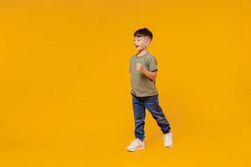 Fototapeta na wymiar Full body side view little small smiling happy boy 6-7 years old wearing green t-shirt walk go strolling isolated on plain yellow background studio portrait Mother's Day love family lifestyle concept