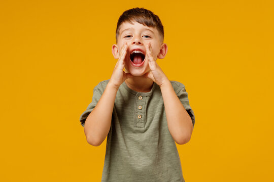 Little small smiling happy boy 6-7 years old in green t-shirt scream hot news about sales discount with hands near mouth isolated on plain yellow background Mother's Day love family lifestyle concept