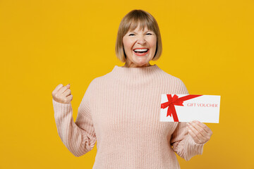 Elderly cool smiling fun woman 50s in pink casual knitted sweater hold gift certificate coupon...