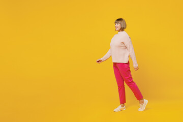 Full body side view elderly smiling happy caucasian woman 50s with bob haircut wears pink casual knitted sweater walk go isolated on plain yellow background studio portrait. People lifestyle concept