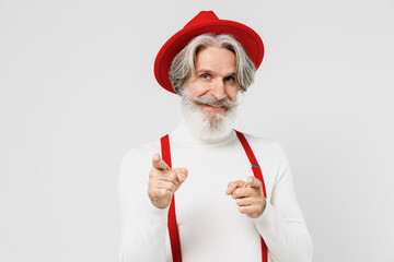 Fototapeta na wymiar Elderly fun gray-haired mustache bearded man 50s in turtleneck red hat suspenders point fingers camera on you motivating isolated on plain white background studio portrait. People lifestyle concept
