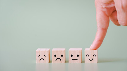human's hand choose smiling face on wooden cube on green background, customer review, feedback,...