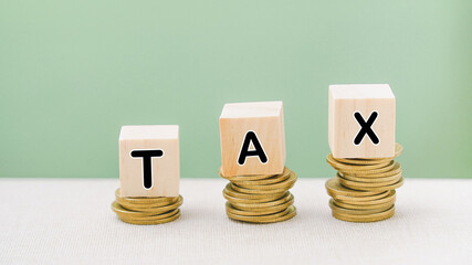 tax word on wooden cubes on stack of coins with green background for business or personal tax payment concept