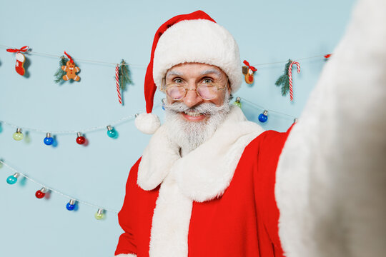 Close up old bearded Santa Claus man 50s in Christmas hat red suit do selfie shot pov on mobile phone isolated on plain blue background studio Happy New Year 2022 celebration merry ho x-mas concept.