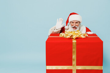 Full size old Santa Claus man 50s in Christmas hat red suit clothes stand near big gift box waving hand isolated on plain blue background studio. Happy New Year 2022 merry ho x-mas holiday concept
