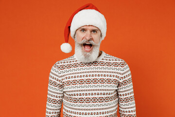 Old displeased irritated sad angry mad bearded dissatisfied Santa Claus man 50s wear Christmas hat sweater posing looking camera scream swear shout call out isolated on plain orange background studio