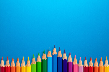 Creative background made of colour pencils on blue paper. Flat lay. Education concept.