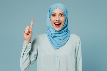 Young arabian asian muslim woman in abaya hijab clothes holding index finger up with great new idea isolated on plain blue background studio portrait People uae middle eastern islam religious concept