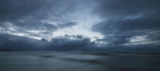 Dark storm sky above the Baltic sea, waves and water splashes. Dramatic cloudscape. Nature, environment, fickle weather, climate change. Atmospheric scenery. Panoramic view, long exposure