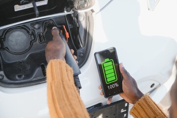 Close up of male hand holding electric charging plug for luxury red car. African businessman charging his auto on station. Eco friendly transport.
