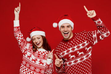 Young cool couple friends two man woman 20s in sweater hat dancing have fun rejoicing isolated on plain red background studio portrait. Happy New Year 2022 celebration merry ho x-mas holiday concept.
