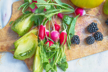 Fresh ripe green tomatoes are cut into slices, cucumber, blackberry, radish on the table. Vegetables from the garden are washed for food