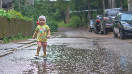 Fototapeta premium Baby girl walks in the rain through puddles in summer