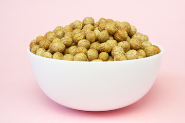 Cereal rye and oats breakfast balls in white ceramic bowl on pink background, side view.