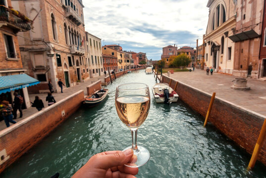 Water canals in Venice and white wine glass in hand of happy tourist
