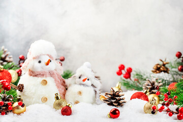 Christmas snow composition with two cute snowmen in hats and scarves in snowdrift and fir branches on gray background