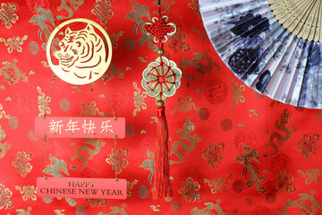 Golden chinese tiger symbol, chinese bamboo paper fan and fortune hunger from lucky coins on red fabric with birds and dragons. Chinese New Year of the Tiger 2022. Translation: happy new year