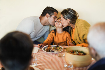 Latin mother and father kissing their daughter during home dinner - Family tender moments concept -...