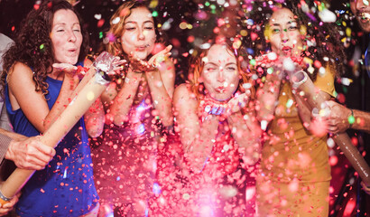 Happy friends celebrating with confetti new year's eve inside disco club - Party concept - Soft focus on left girl hand