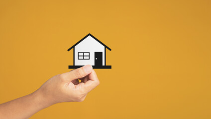 Fototapeta na wymiar Business and real estate concept. Close-up of hand holding a mini paper house while standing on a yellow background in the studio. Space for text. Property insurance and security