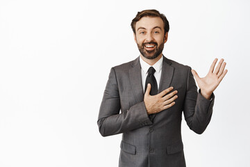 Portrait of corporate man raising palm, put hand on heart and smiling sincere, making promise, introduce himself, standing in grey suit over white background