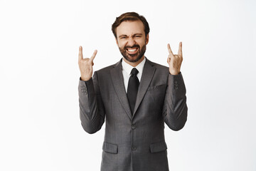Lets rock. Happy corporate man in office suit showing horns gesture, heavy metal and smiling pleased, rejoicing, standing over white background