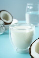 Coconut products. Cracked open coconut with meat cut in half, coconut powder in a glass jar, plant milk on a blue background. isometric projection. Copy space. Concept alternative milk, vegeterian
