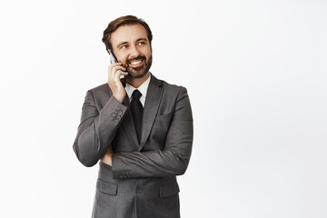 Handsome realtor smiling, talking on mobile phone and looking at upper right corner empty space, banner, standing over white background