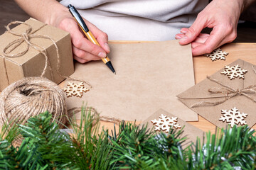 Hand writing a letter with a pen on blank recycled paper on a table with fir with pine cones,...
