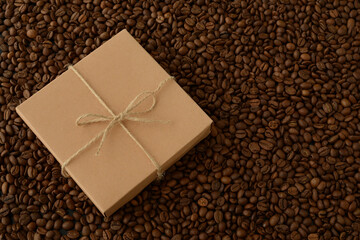 Beautiful gift and coffee grains. Brown gift box with a bow on the background of the texture of coffee beans. An original gift or present for coffee lovers. Flat lay, space for text